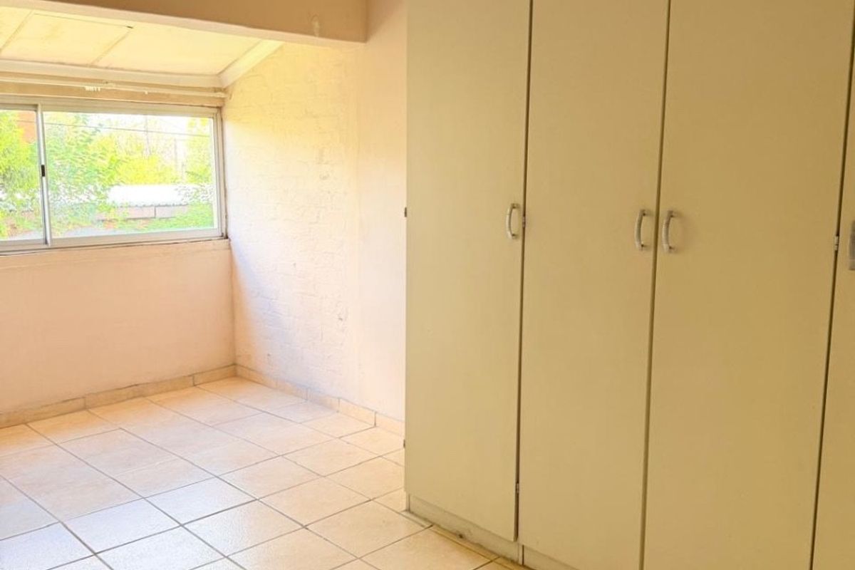 A bedroom featuring built-in cupboards, tiled flooring, and a window providing natural light.