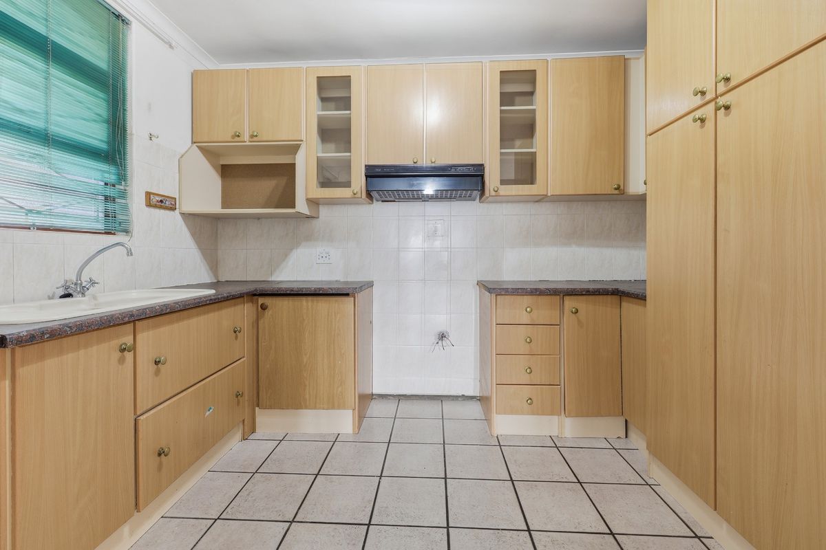 A functional kitchen featuring light wood-finish cabinetry, tiled flooring, a double sink, and an integrated extractor fan, awaiting new appliances.