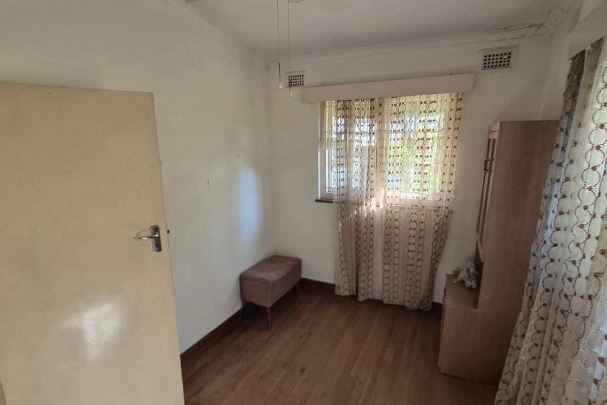 A bedroom featuring wood-look flooring, a window with curtain treatments, and a ceiling vent, showing signs of wear and dated finishes.