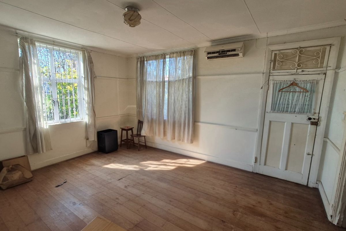 A spacious living room featuring original timber flooring, security bars on windows, and a wall-mounted air conditioning unit.
