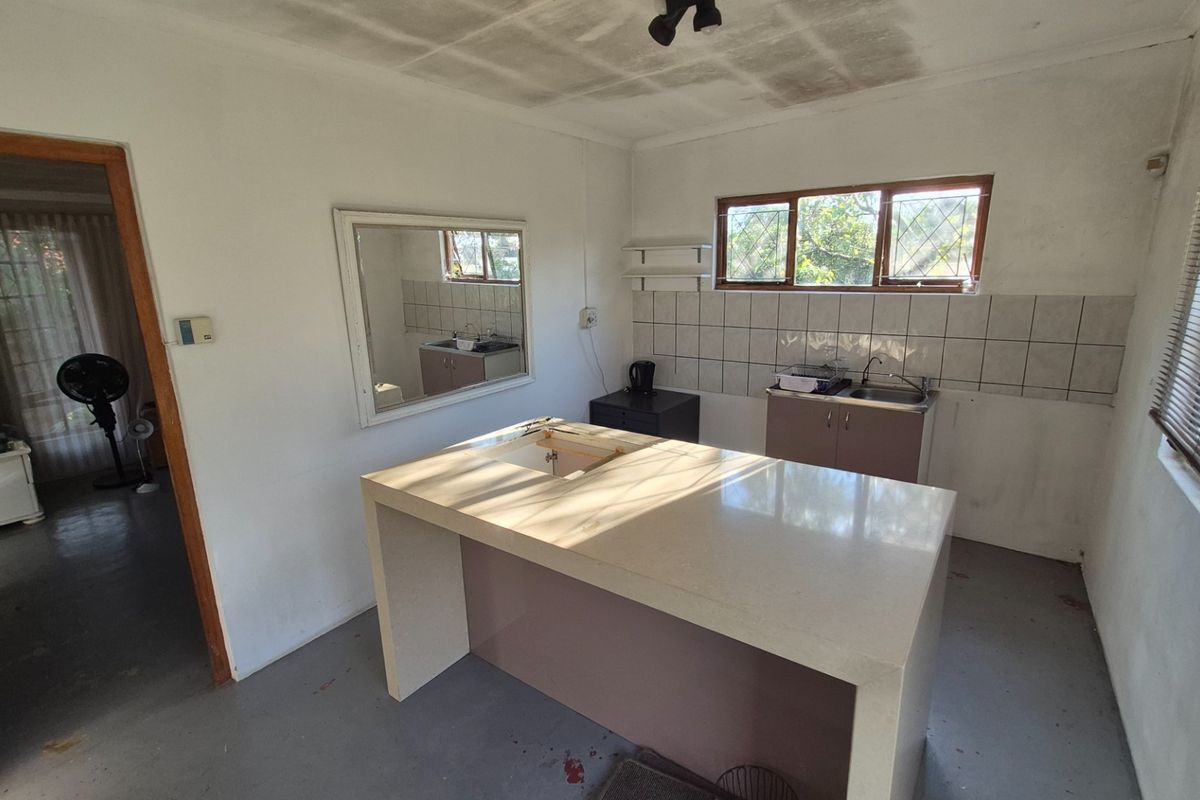 A dated kitchen space featuring a central island, tiled splashback, and sink area, requiring renovation to modernize the finishes and improve functionality.