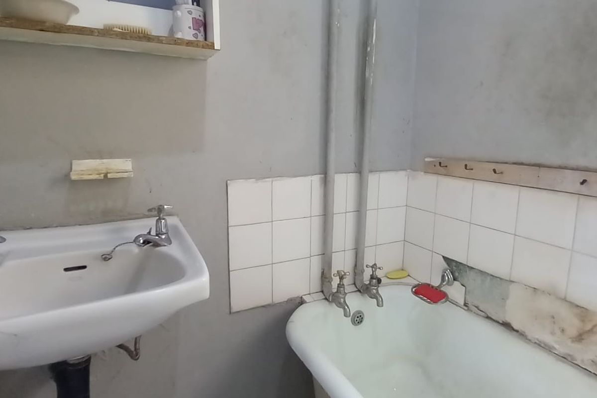 A dated bathroom featuring a pedestal basin and a cast iron bathtub with exposed plumbing, requiring significant renovation and cosmetic updates.