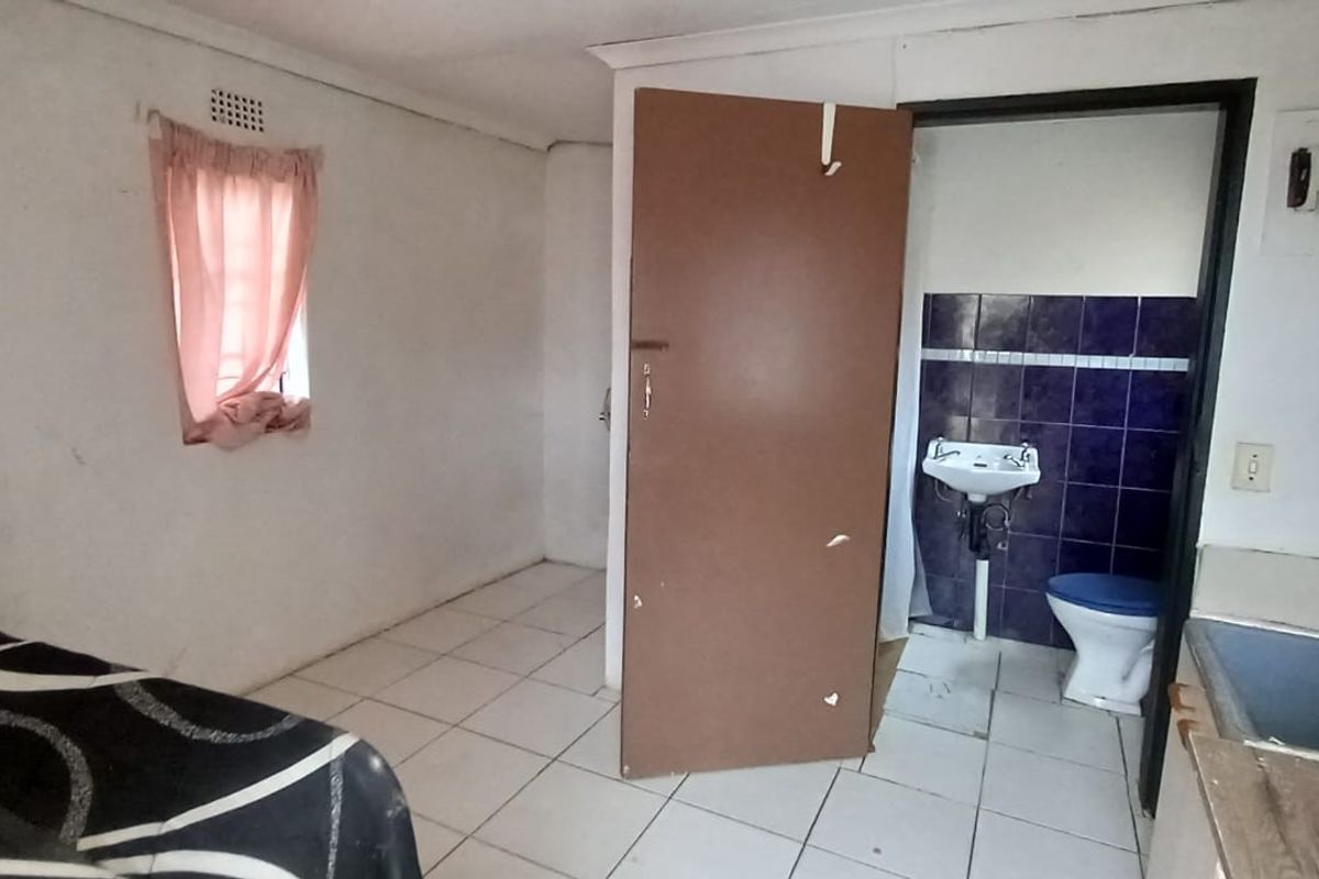 A bedroom featuring tiled flooring and an attached small bathroom area with a basin and toilet, requiring cosmetic updates to improve the space.