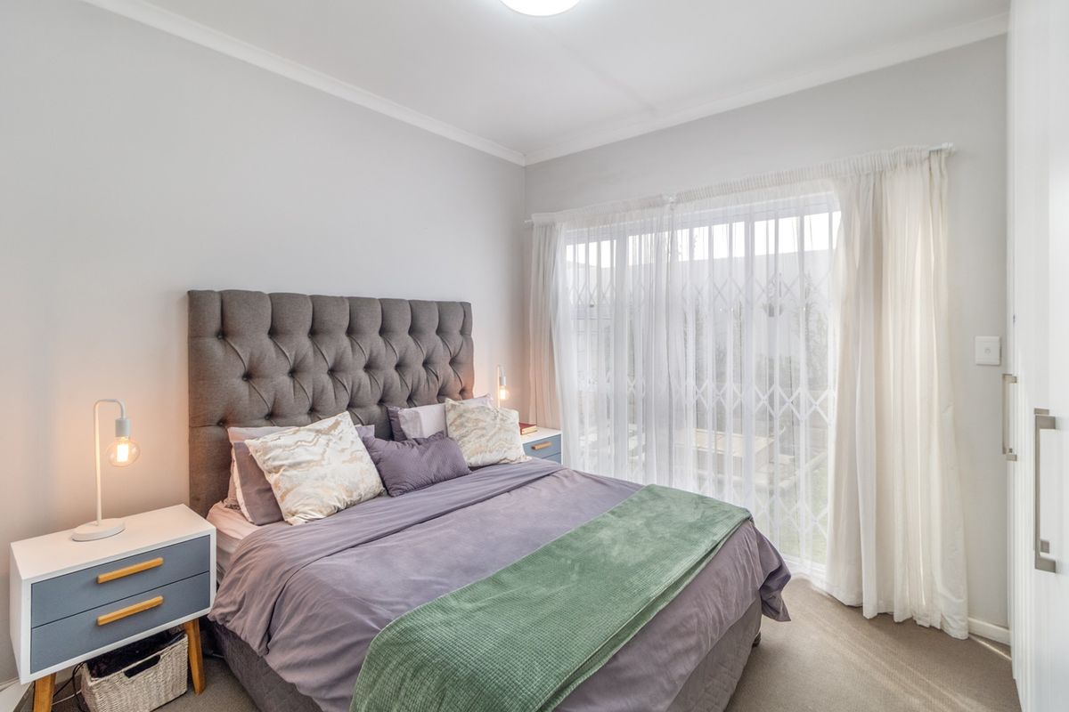 A well-maintained bedroom featuring neutral wall tones, carpeted flooring, and a large sliding door with security gate providing access to the exterior.
