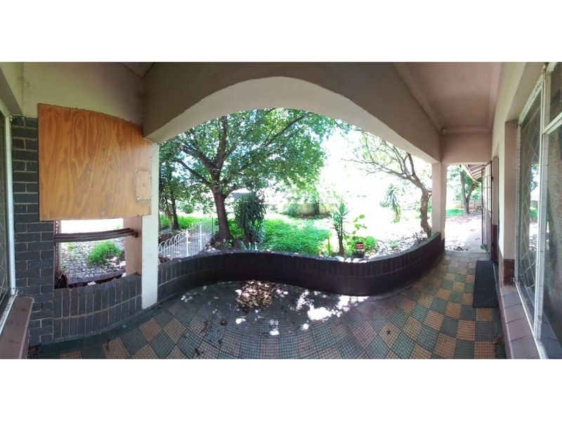 A covered patio area featuring a curved brick wall, tiled flooring, and views overlooking the garden, requiring maintenance and repair.