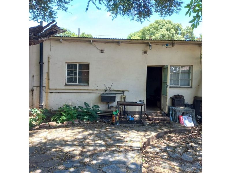Rear exterior view of the property featuring a paved patio area, weathered facade, and access door.
