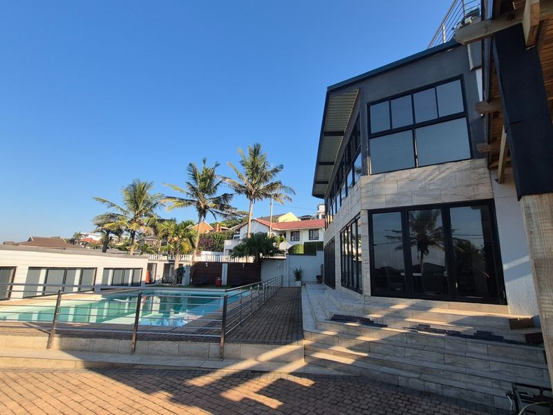 Modern multi-level home exterior featuring a swimming pool, paved patio area, large glass windows, and contemporary architectural finishes.