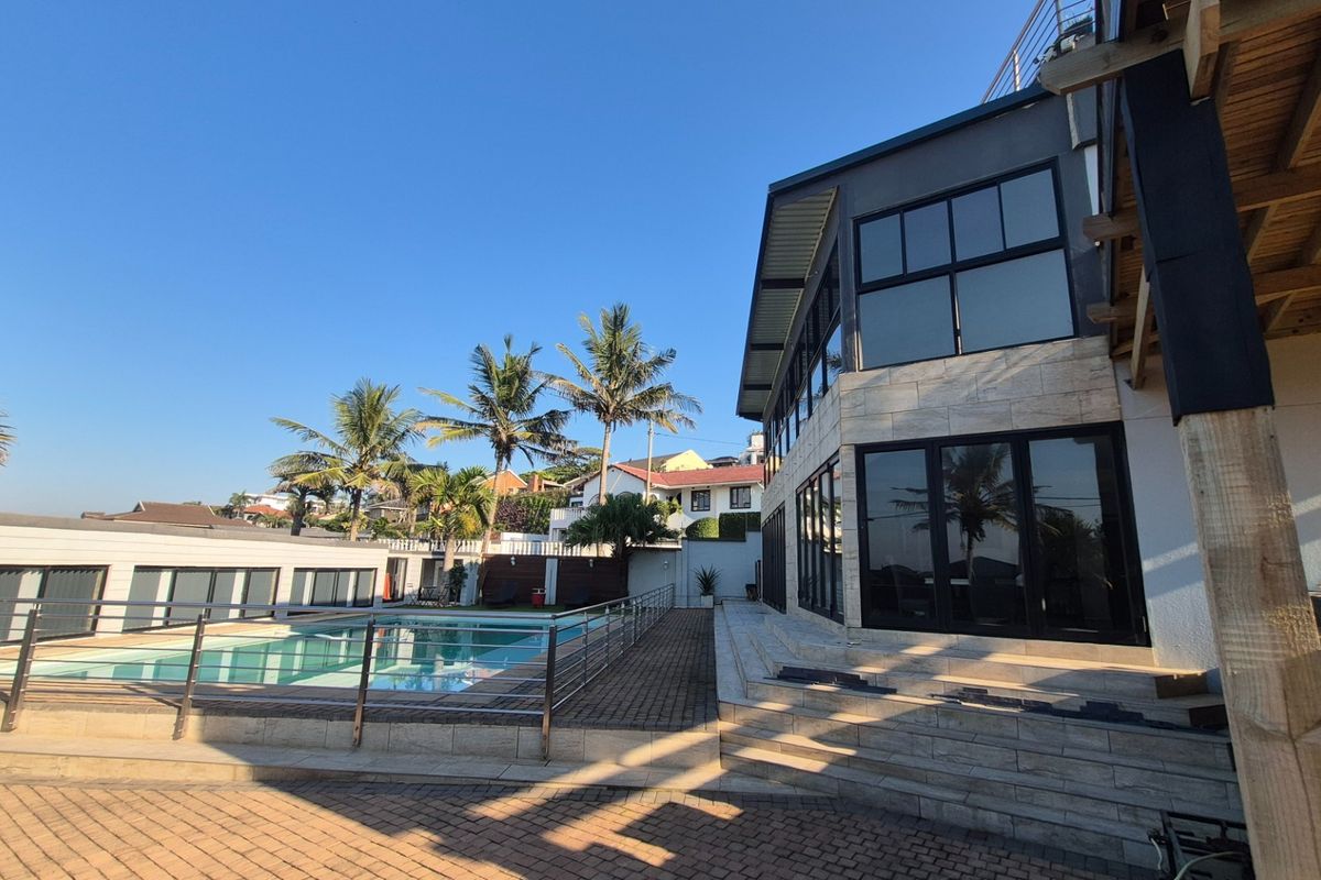 Modern multi-level home exterior featuring a swimming pool, paved patio area, large glass windows, and contemporary architectural finishes.