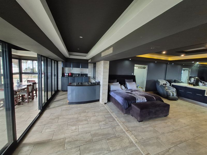 Spacious open-plan bedroom suite featuring a modern kitchenette, tiled flooring, recessed ceiling lighting, and large sliding glass doors leading to an outdoor patio area.