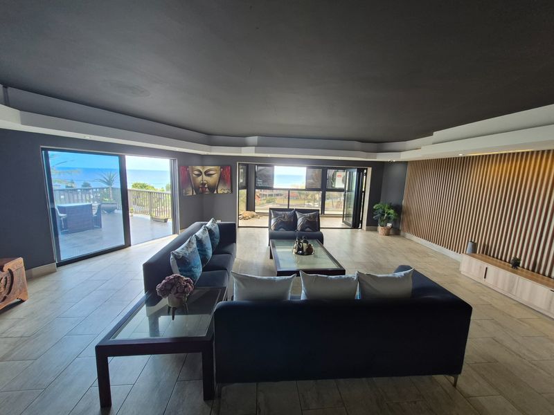 Spacious living area featuring modern tiled flooring, decorative timber slat wall paneling, and large sliding glass doors opening to an outdoor balcony with ocean views.