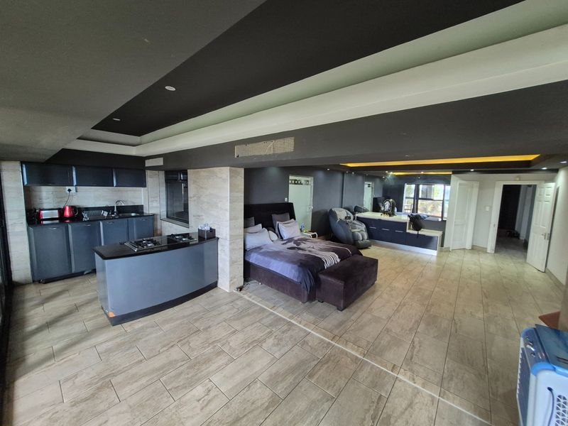 An open-plan studio space featuring a modern kitchen with dark cabinetry, a central island with a built-in hob, and integrated bedroom area.