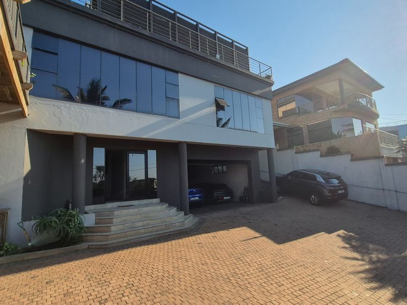 Modern multi-story residential property featuring a paved driveway, integrated garage, and large glass facade elements with a balcony.