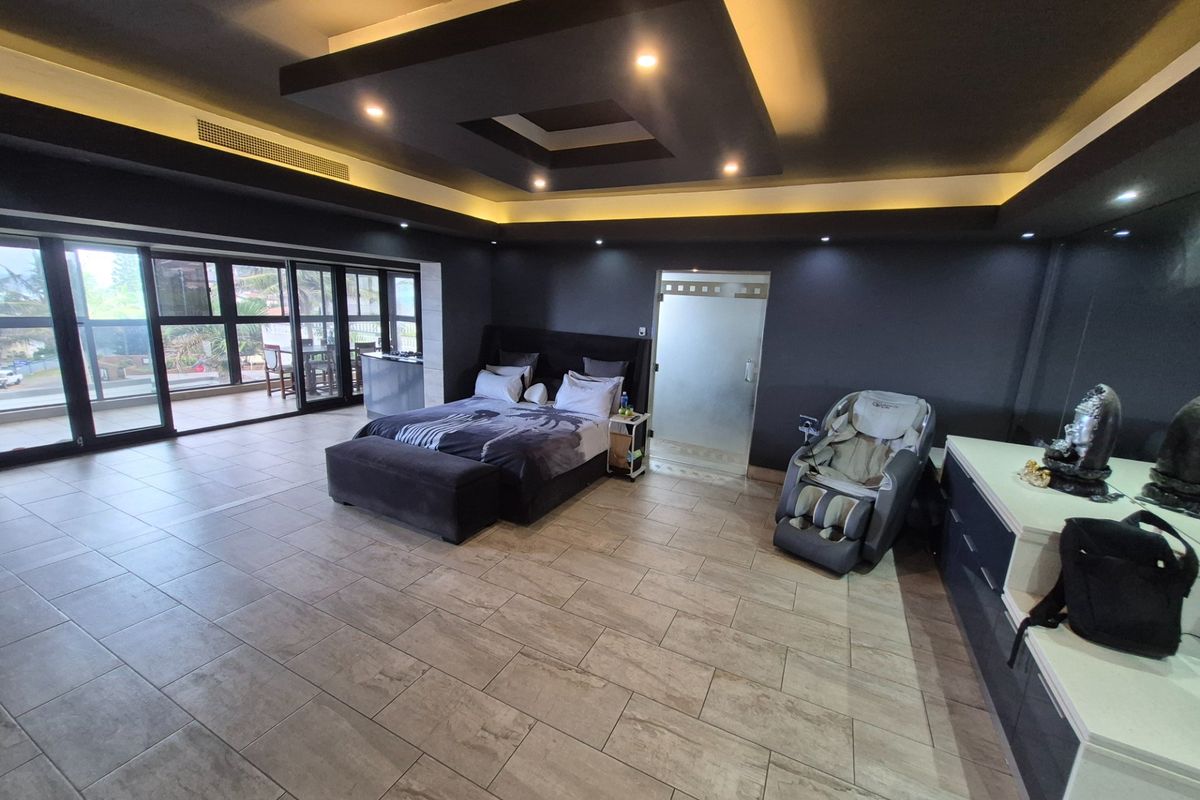 Spacious modern bedroom featuring a coffered ceiling with recessed lighting, large sliding glass doors leading to a balcony, and tiled flooring.