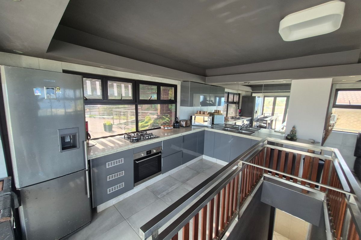 Modern kitchen featuring sleek grey cabinetry, stone countertops, built-in oven, gas hob, and large windows overlooking the exterior.