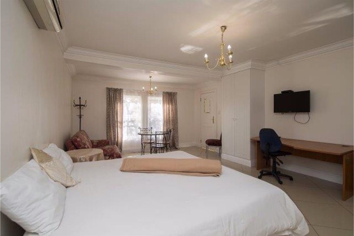 A spacious bedroom featuring built-in cupboards, tiled flooring, crown molding, and a wall-mounted air conditioning unit.