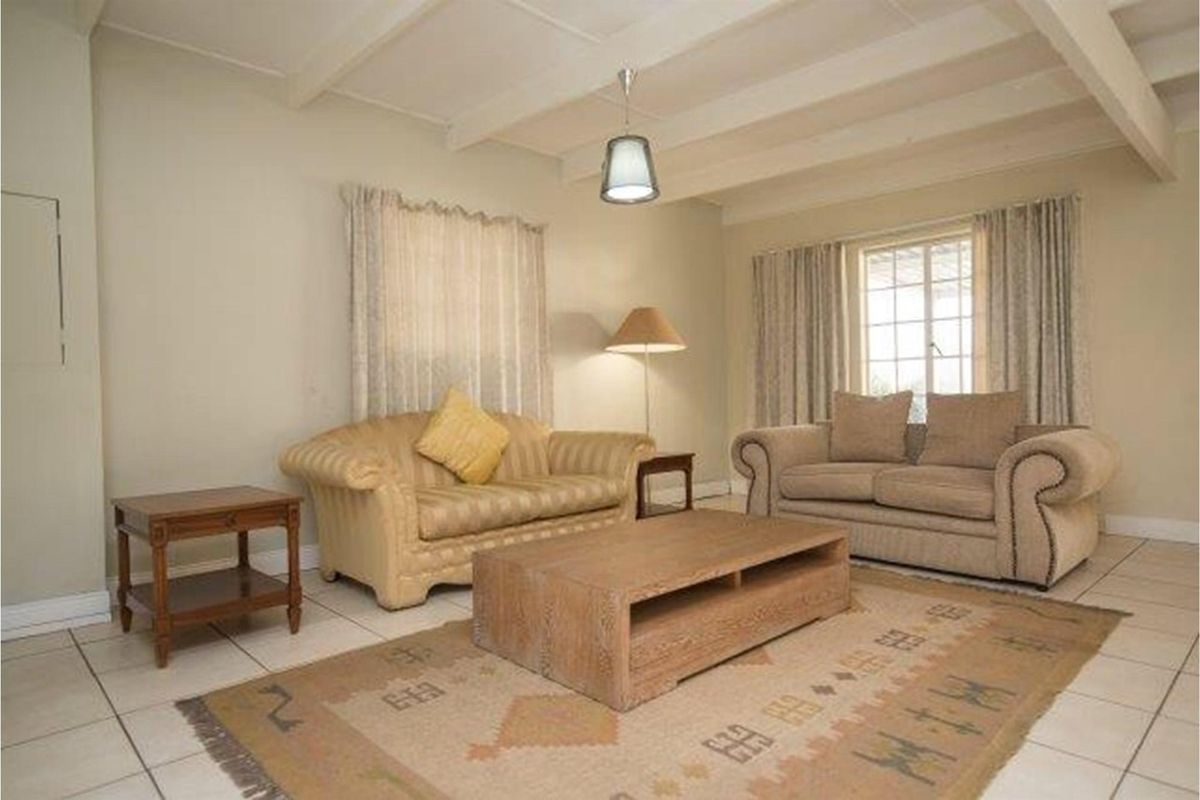 A comfortable living room featuring exposed ceiling beams, tiled flooring, and large windows that provide ample natural light.