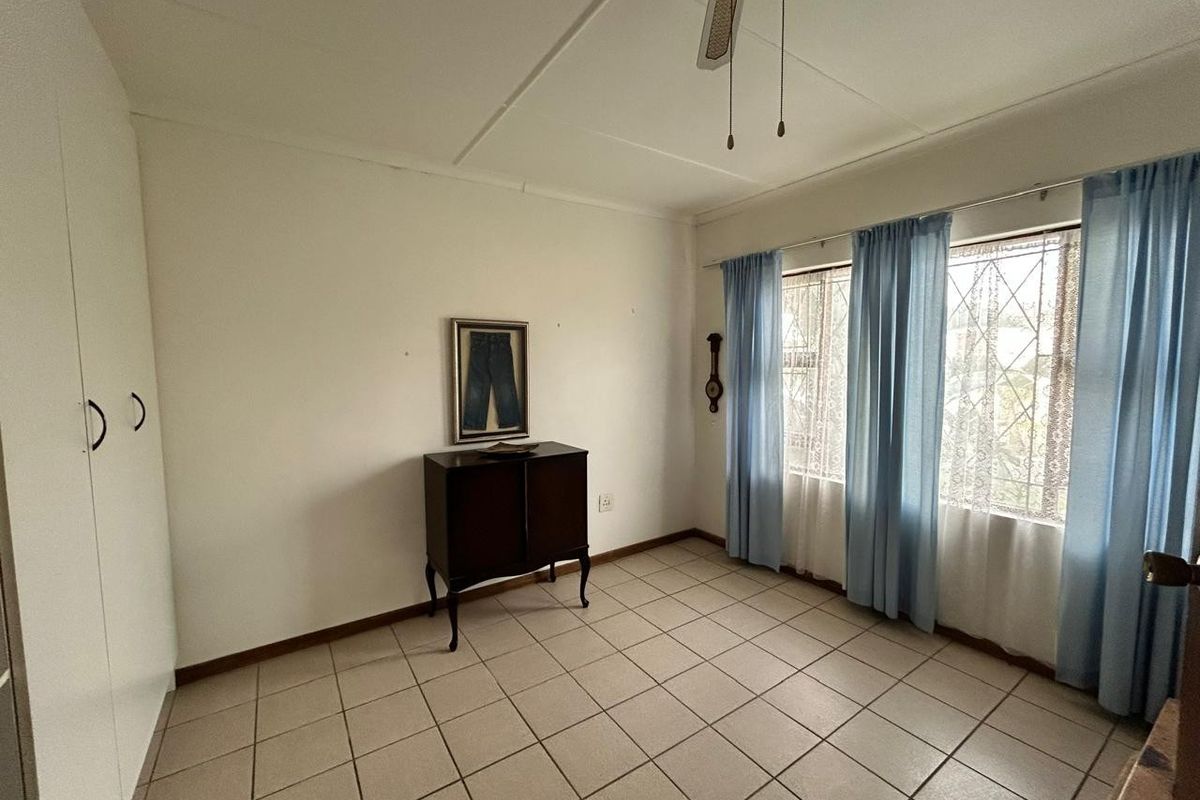A bedroom featuring tiled flooring, built-in cupboards, a ceiling fan, and security bars on the windows.