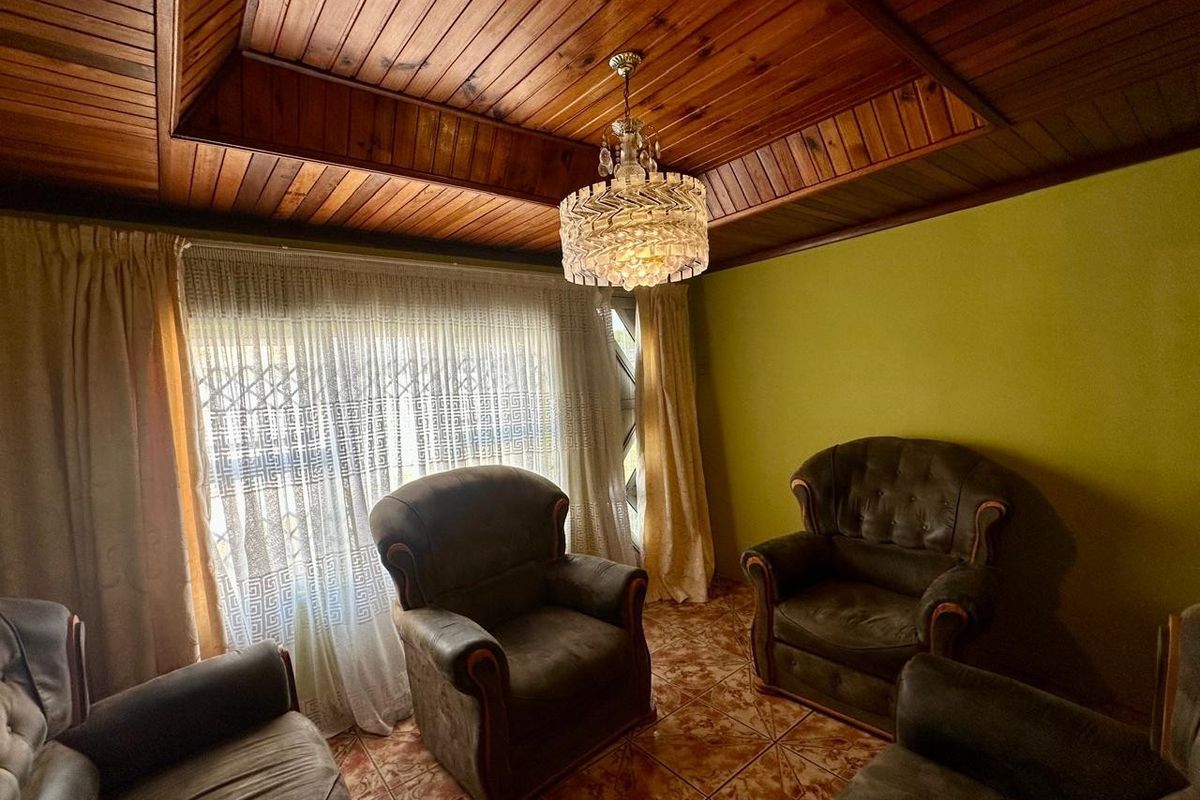 A living room featuring a traditional wood-paneled tray ceiling, tiled flooring, and a decorative crystal chandelier.