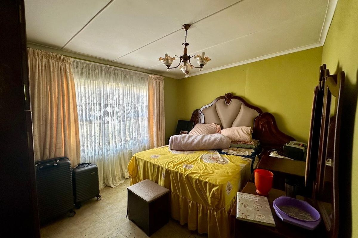 A bedroom featuring a central chandelier, large window with curtains, and tiled flooring, requiring cosmetic updates to modernize the space.