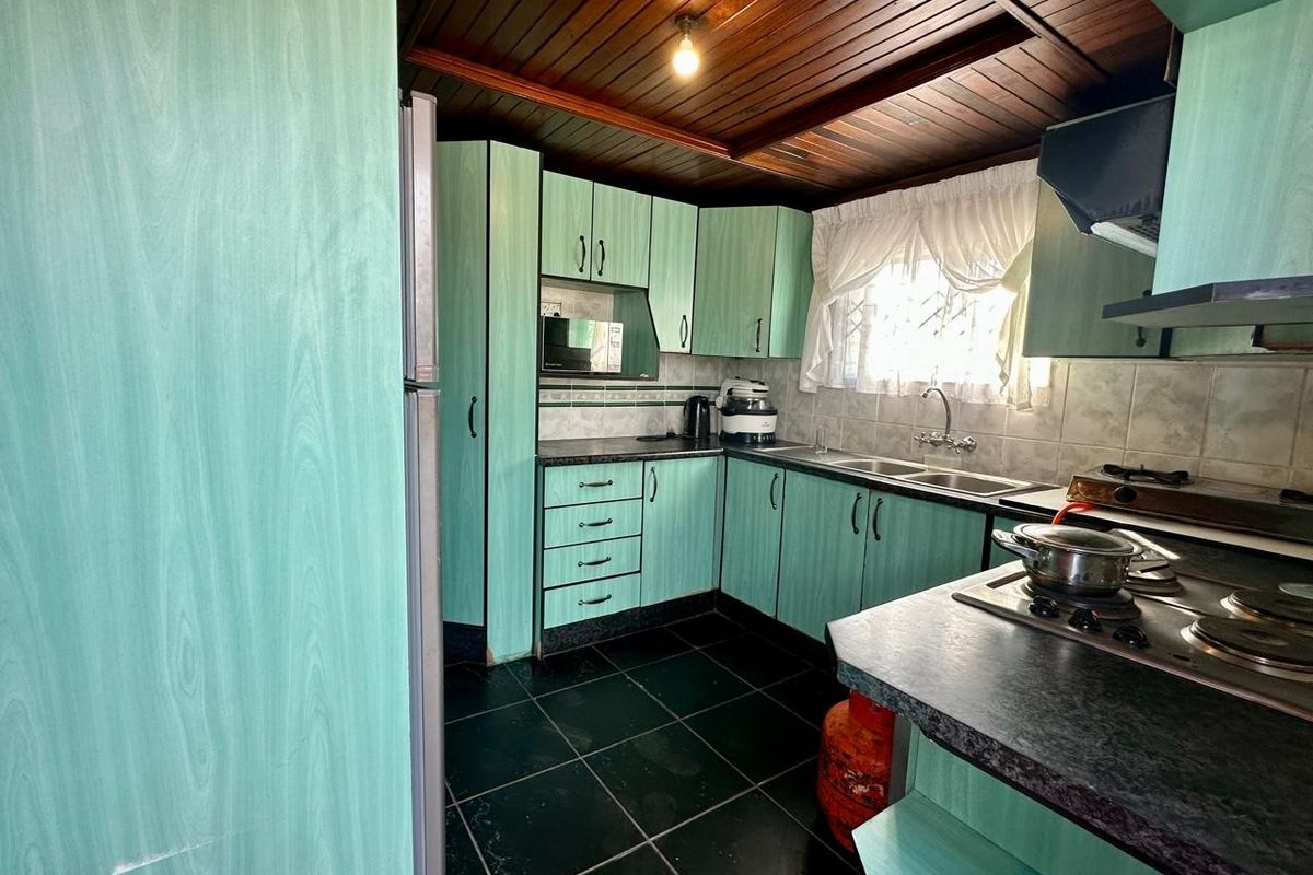 A functional kitchen featuring mint-green cabinetry, dark tiled flooring, a timber-paneled ceiling, and integrated gas hob and sink area.
