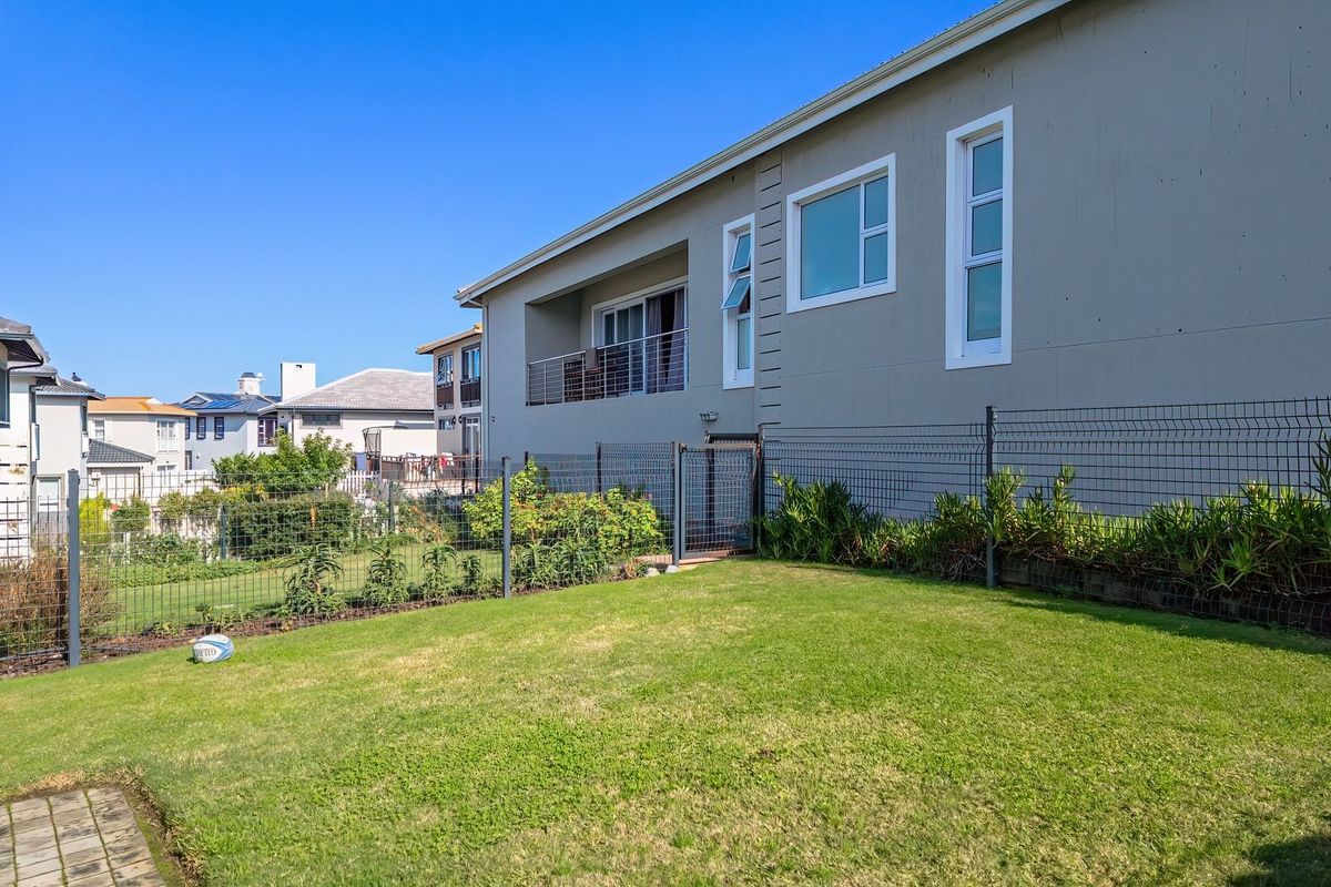 A view of the rear exterior of the house, featuring a landscaped lawn, wire mesh fencing, and an upper-level balcony.