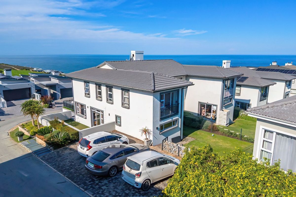 Aerial view of a modern two-story residential property featuring a tiled roof, paved driveway, and landscaped garden, situated in a coastal estate.