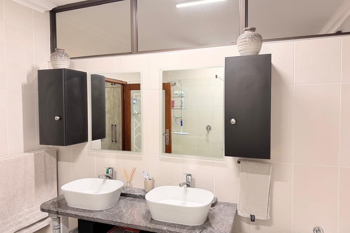 A modern bathroom featuring a double vanity with vessel sinks, granite countertop, wall-mounted storage cabinets, and large mirrors.