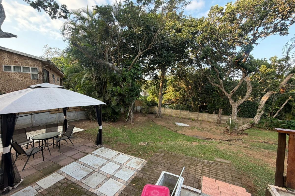 A spacious rear garden featuring a paved patio area, mature trees, and a perimeter boundary wall, offering a private outdoor space.