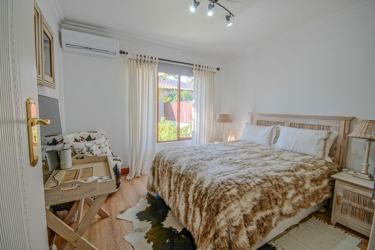 A well-maintained bedroom featuring laminate flooring, a wall-mounted air conditioning unit, and large windows allowing for natural light.