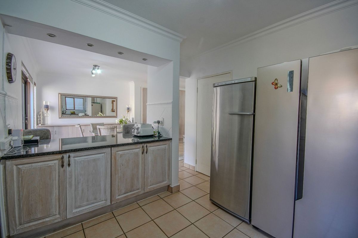 A functional kitchen featuring granite countertops, light-toned cabinetry, and tiled flooring, with an open-plan layout connecting to the adjacent dining area.