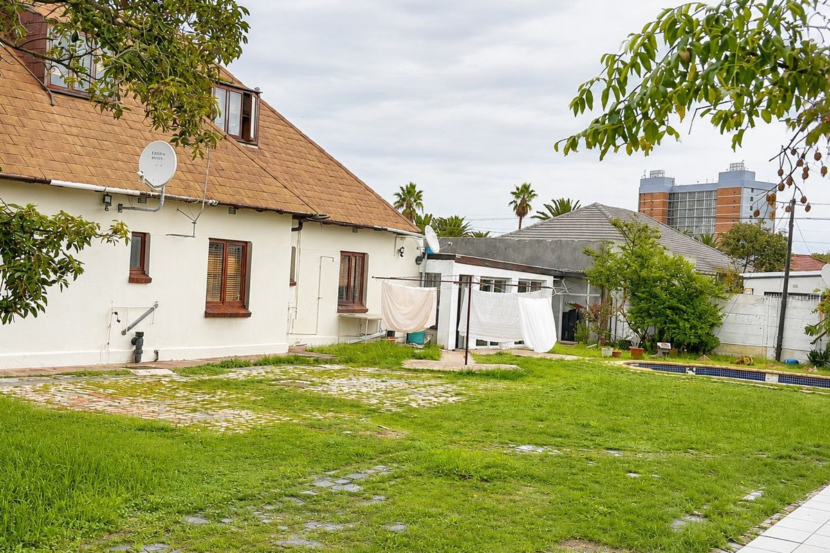 Rear view of the property featuring a spacious garden, swimming pool, and paved area adjacent to the main dwelling structure.
