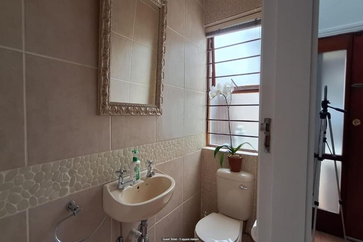 A compact guest bathroom featuring neutral wall tiling with a decorative pebble-style border, a wall-mounted basin, and a standard toilet.