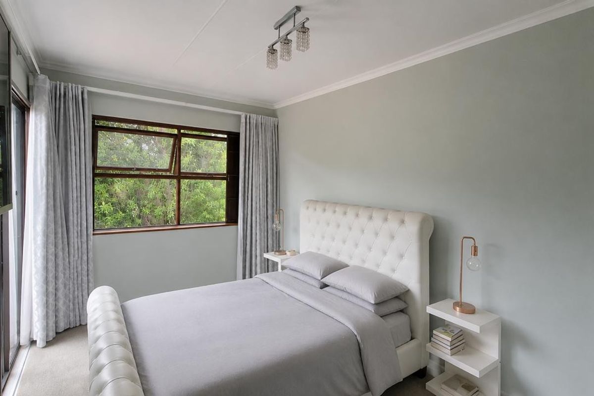 A well-maintained bedroom featuring neutral wall tones, carpeted flooring, and a large window providing natural light and garden views.