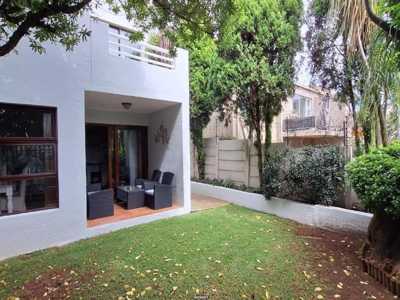 A private rear garden featuring a covered patio area, established trees, and perimeter walling, providing a quiet outdoor space for the townhouse.