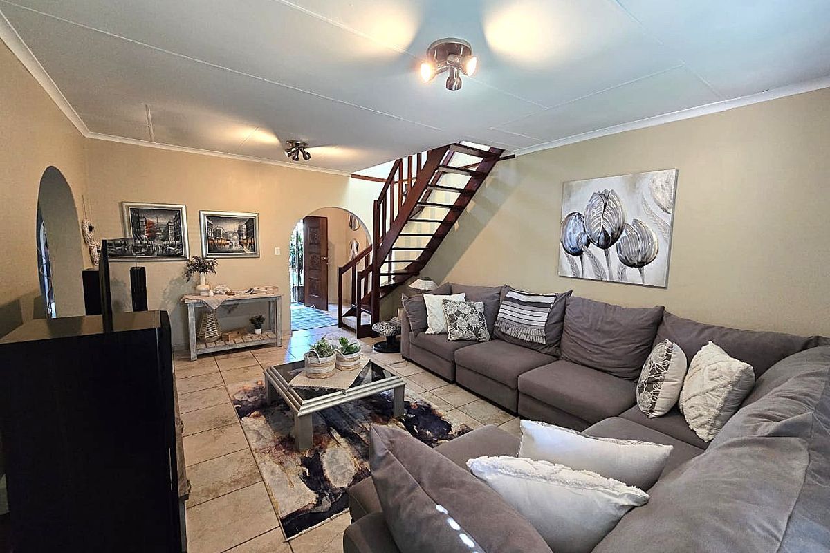 Spacious living room featuring tiled flooring, a wooden staircase, and arched entryways leading to adjacent areas.