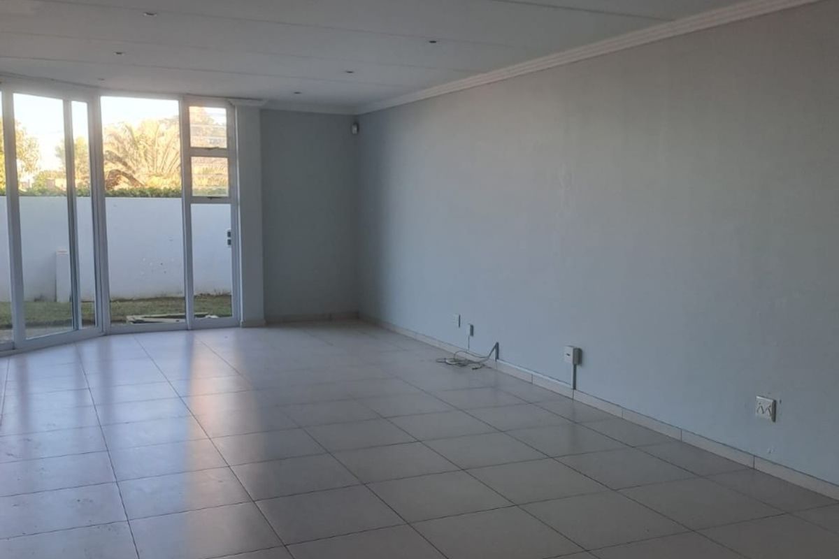 A spacious, empty living area featuring neutral tiled flooring, recessed downlighting, and large sliding glass doors providing access to the exterior.