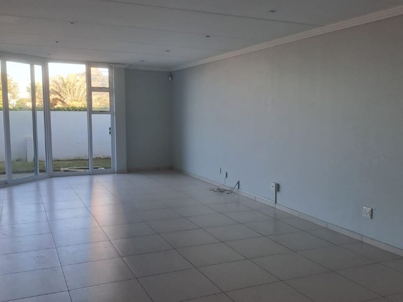A spacious, empty living area featuring neutral tiled flooring, recessed downlighting, and large sliding glass doors providing access to the exterior.