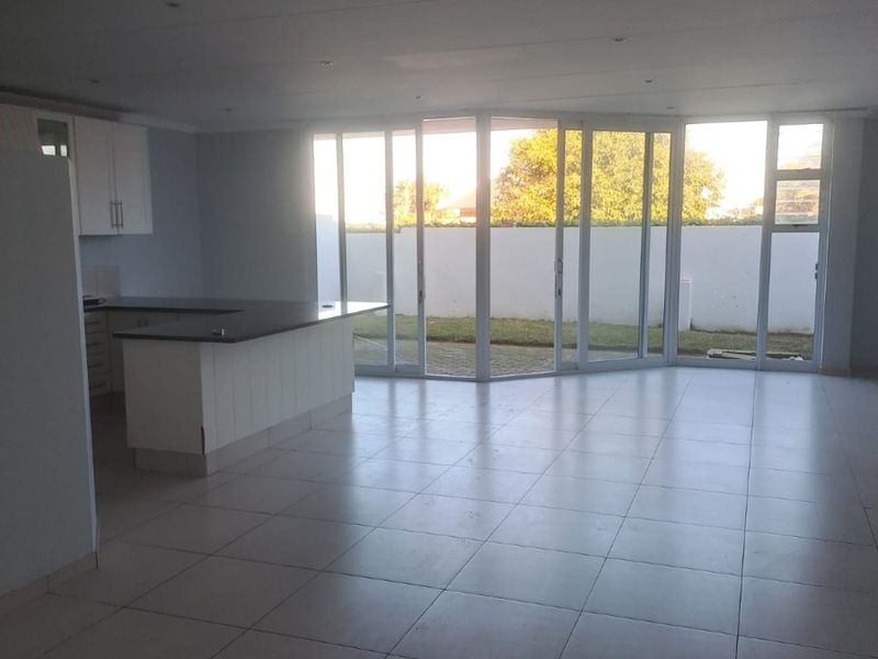 Spacious open-plan living and kitchen area featuring tiled floors, modern cabinetry, and large sliding glass doors opening to the rear garden.