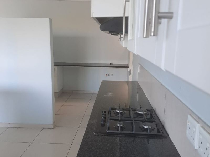 A clean, modern kitchen featuring dark granite countertops, a built-in gas hob, extractor fan, and white cabinetry, presented in an empty, move-in ready state.