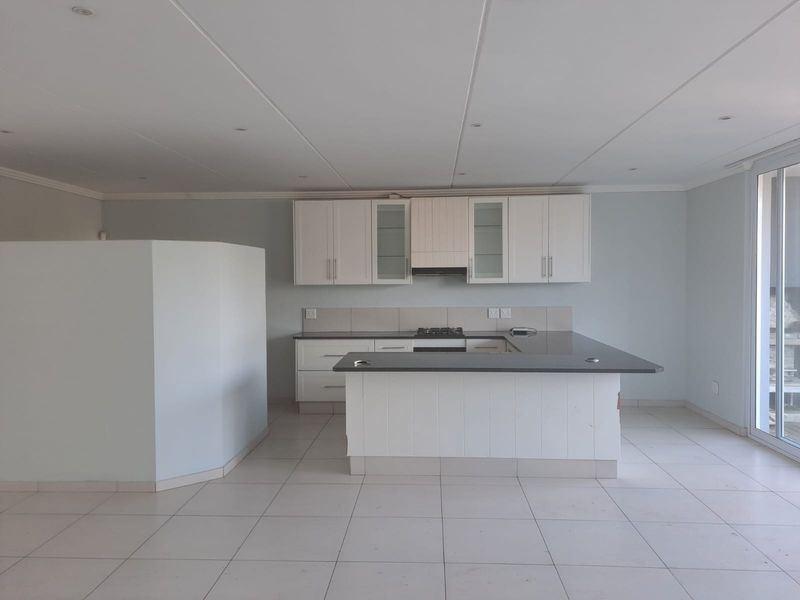 A clean, empty kitchen featuring white cabinetry, dark stone countertops, a gas hob with extractor, and a functional breakfast bar island.