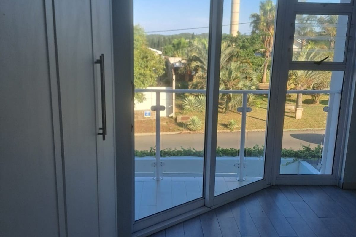 A bright, empty bedroom featuring modern laminate flooring, built-in wardrobes, and a sliding glass door leading to a private balcony with a glass balustrade.