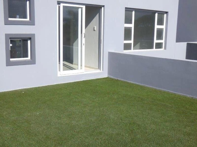 A neat rear exterior area featuring a low boundary wall, artificial turf, and access to the interior via a sliding glass door.