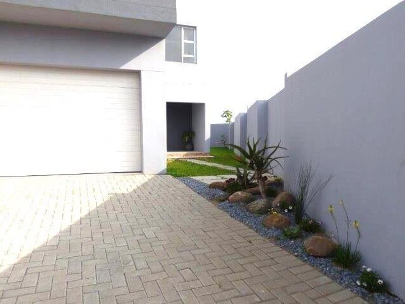 Modern front exterior featuring a paved driveway, automated garage door, and a neat landscaped garden bed along the boundary wall.