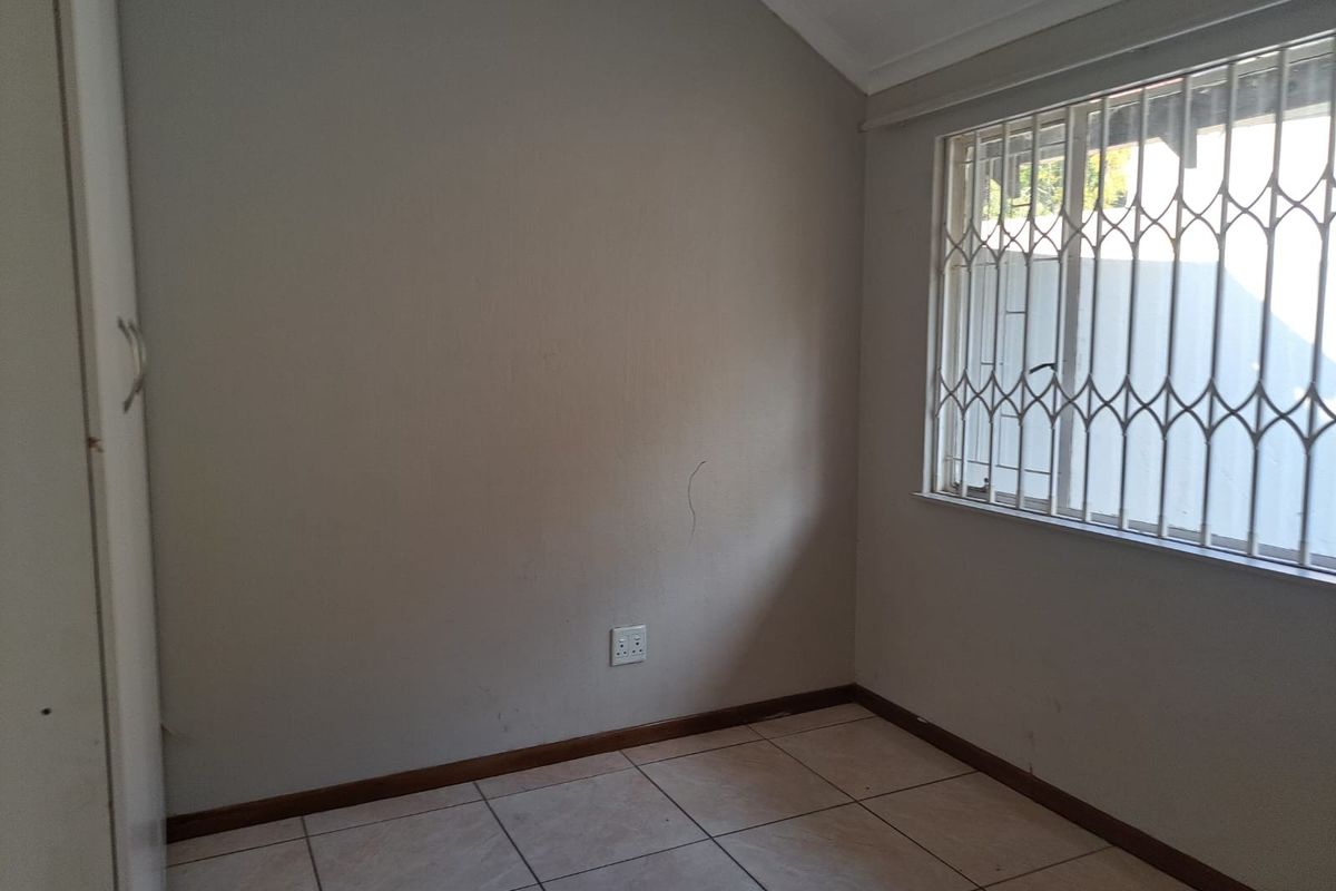 An empty bedroom featuring tiled flooring, a built-in cupboard, and a window fitted with a security gate.