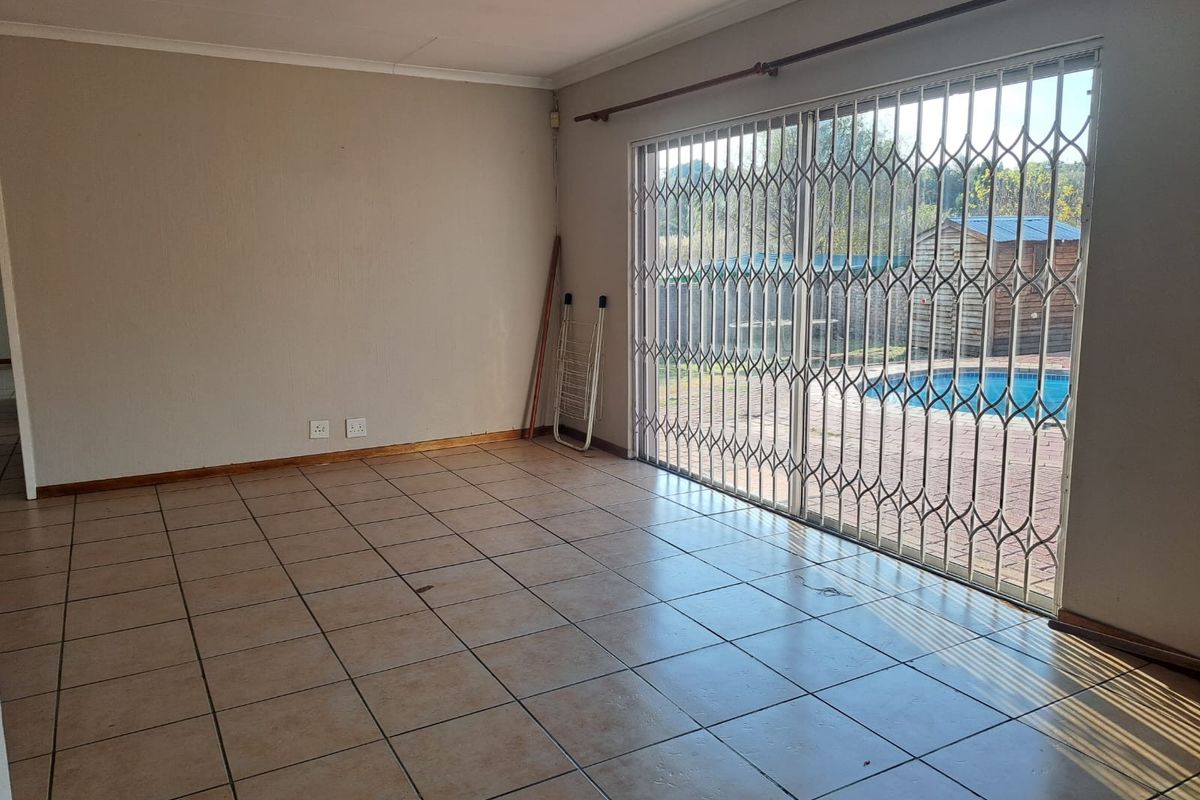 An empty living room featuring tiled flooring and a large sliding glass door with a security gate, providing direct access to the pool area.
