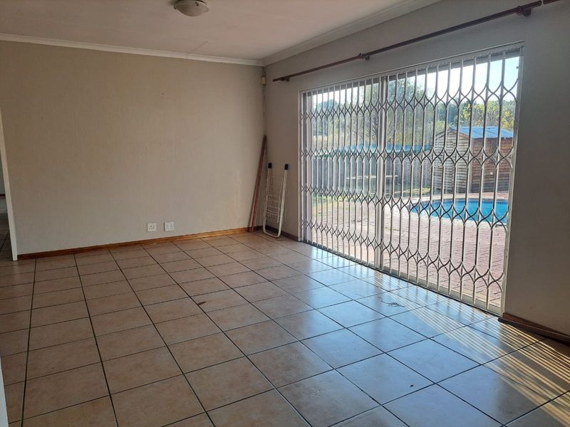 An empty living room featuring tiled flooring and a large sliding glass door with a security gate, providing direct access to the pool area.
