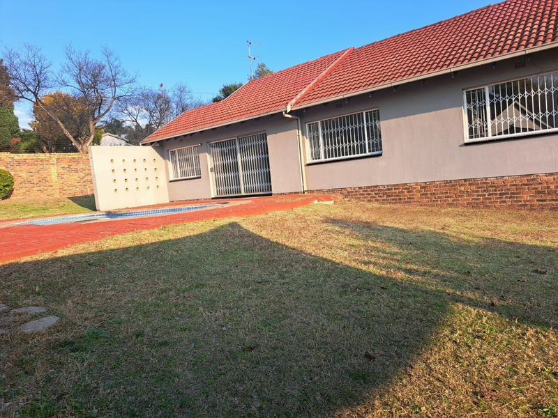 Rear view of the house featuring a tiled roof, swimming pool, and a spacious garden area with security gates on windows and doors.
