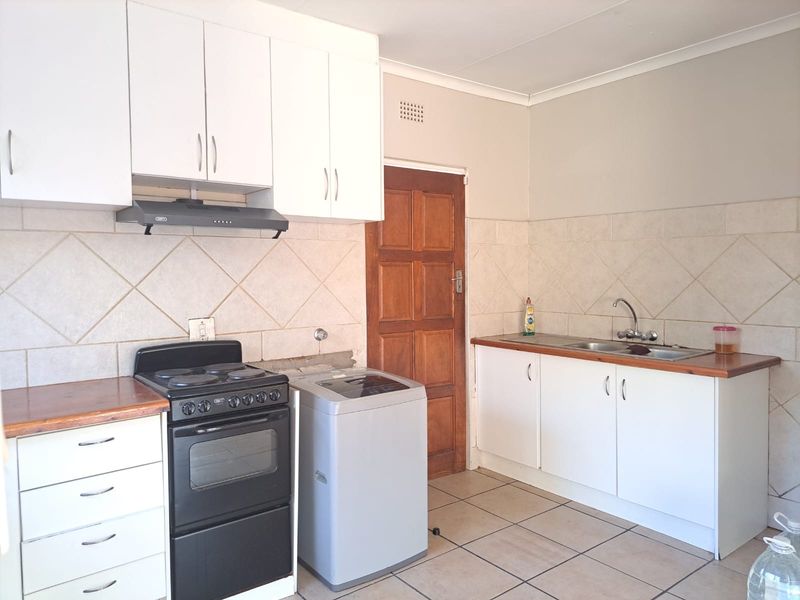 Functional kitchen featuring white cabinetry, tiled splashbacks, double sink, and tiled flooring, with a dedicated space for a freestanding stove and laundry appliance.