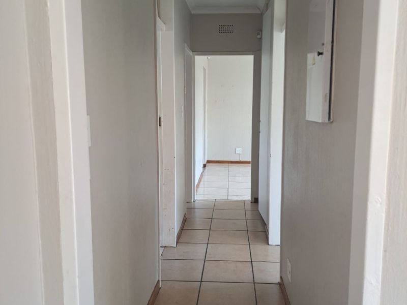 A functional, tiled hallway providing access to multiple rooms, featuring neutral wall tones and a ceiling access hatch.