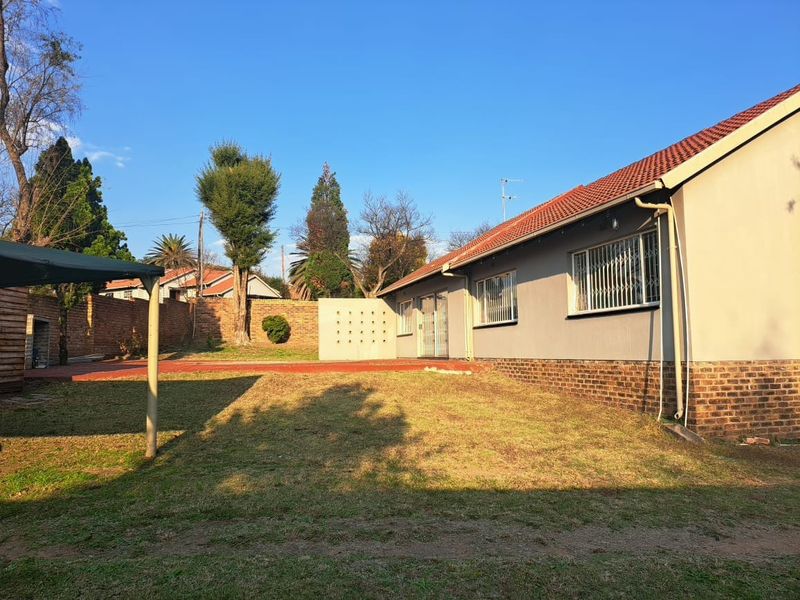 Rear view of the property featuring a paved patio area, brick boundary wall, and a spacious garden with established trees.